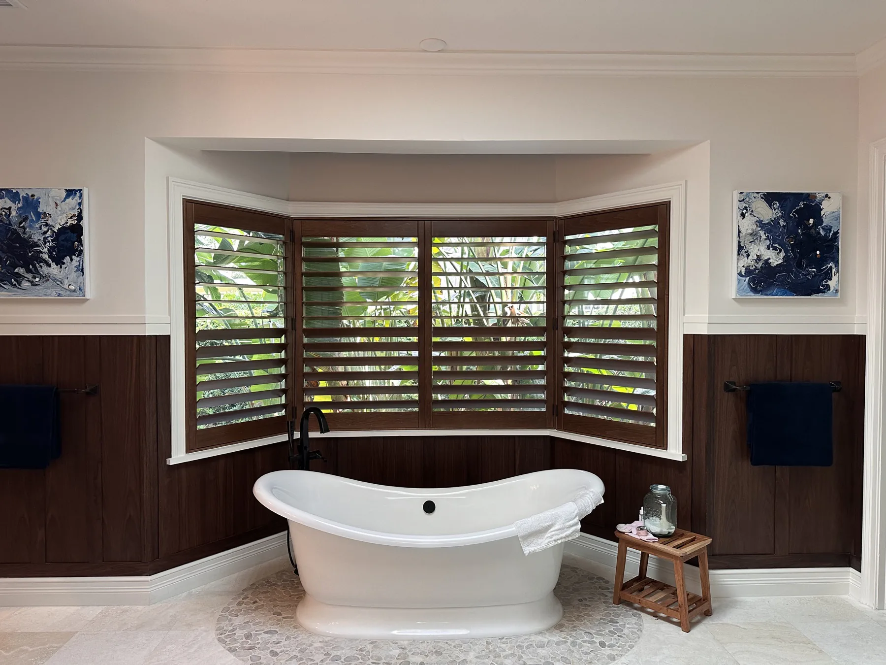 Dark wood plantation shutters fitted to a wide bay window above a bathtub
